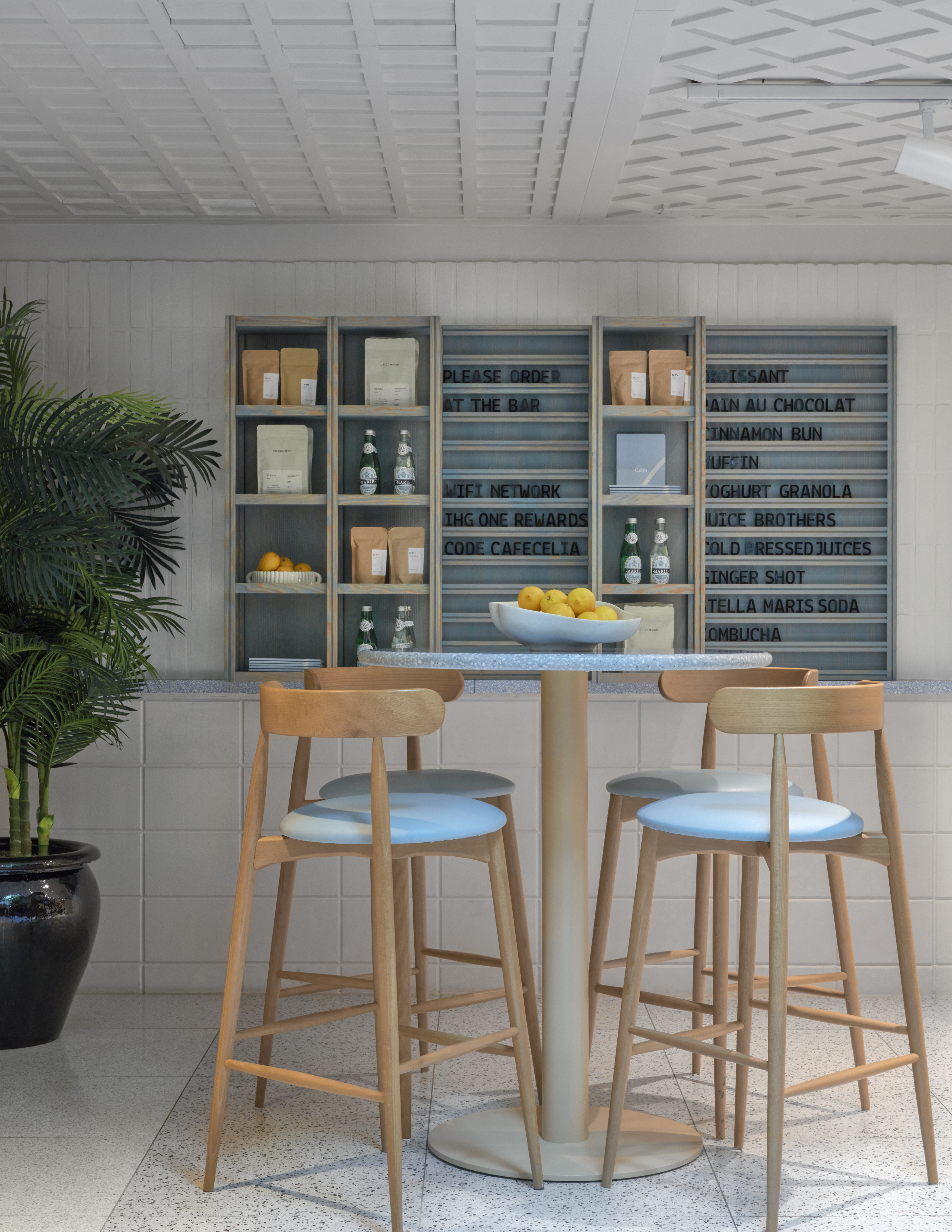 A modern café corner with a menu board, plant, and a table set with drinks and snacks at Café Celia in Amsterdam.