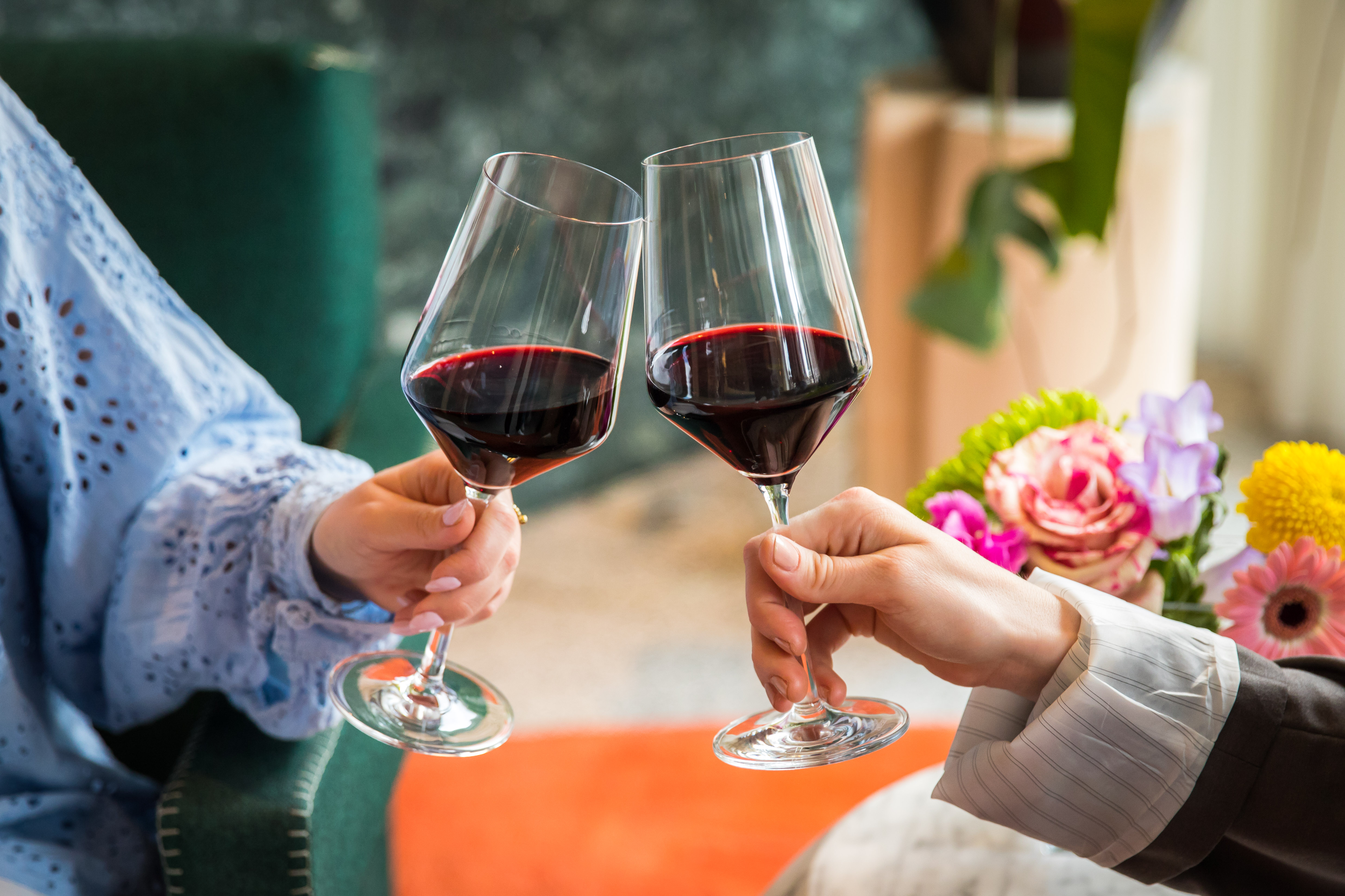 Toasting with glasses of red wine, surrounded by vibrant flowers and greenery at the stylish restaurant, Celia Amsterdam.