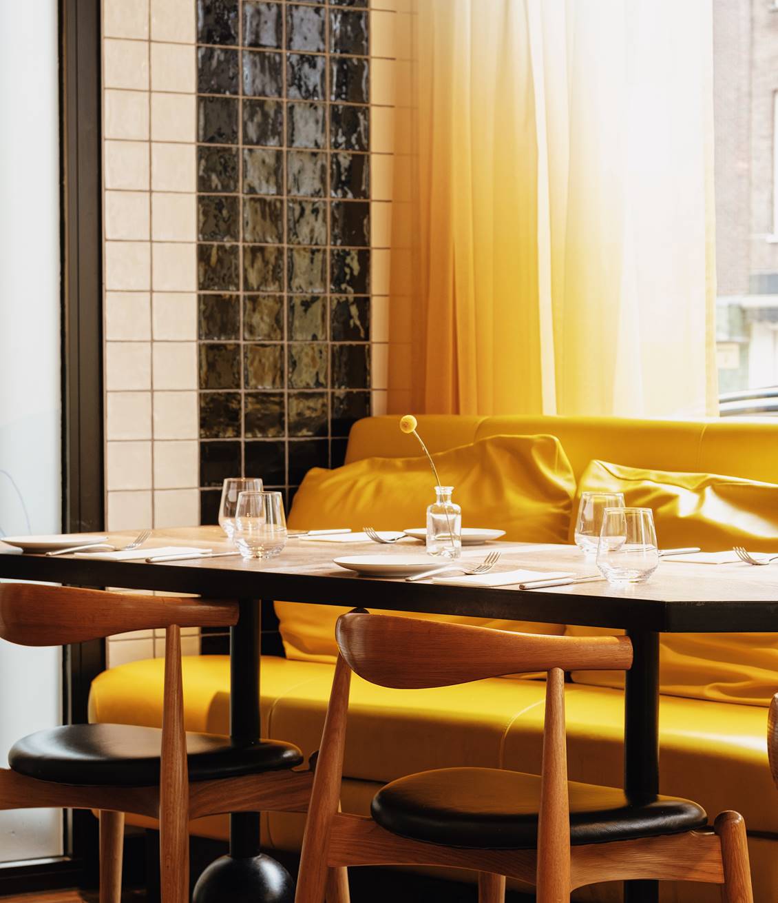 An intimate table setup with a yellow couch and cushions, glassware, and a small flower vase at Celia Amsterdam.