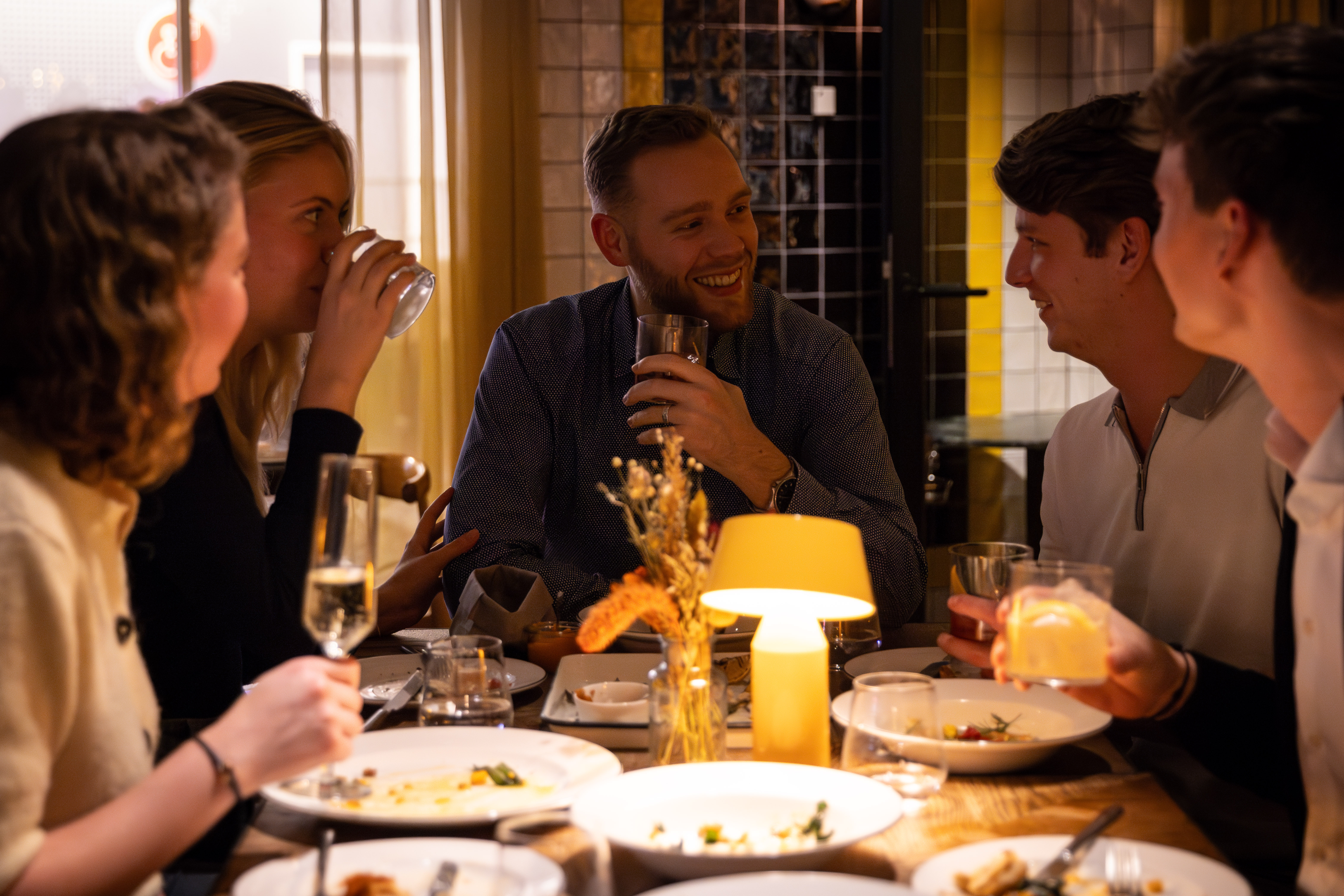 A group of friends laughing and enjoying drinks together at a table at Celia restaurant in Amsterdam.