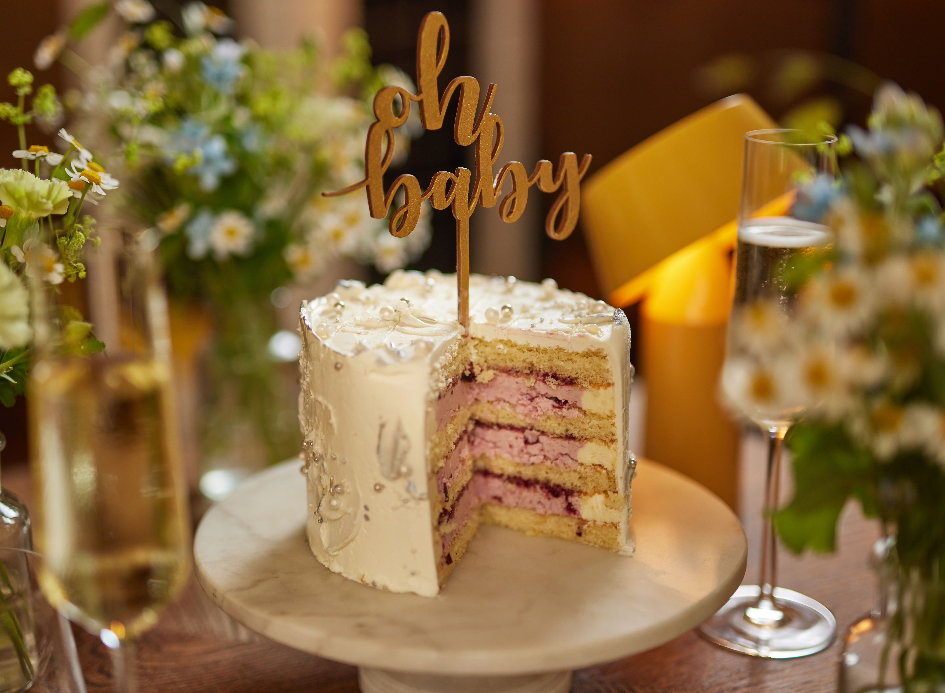 A decorated "Oh Baby" cake with pink filling and white icing, flowers and drinks at a baby shower at Celia Amsterdam.