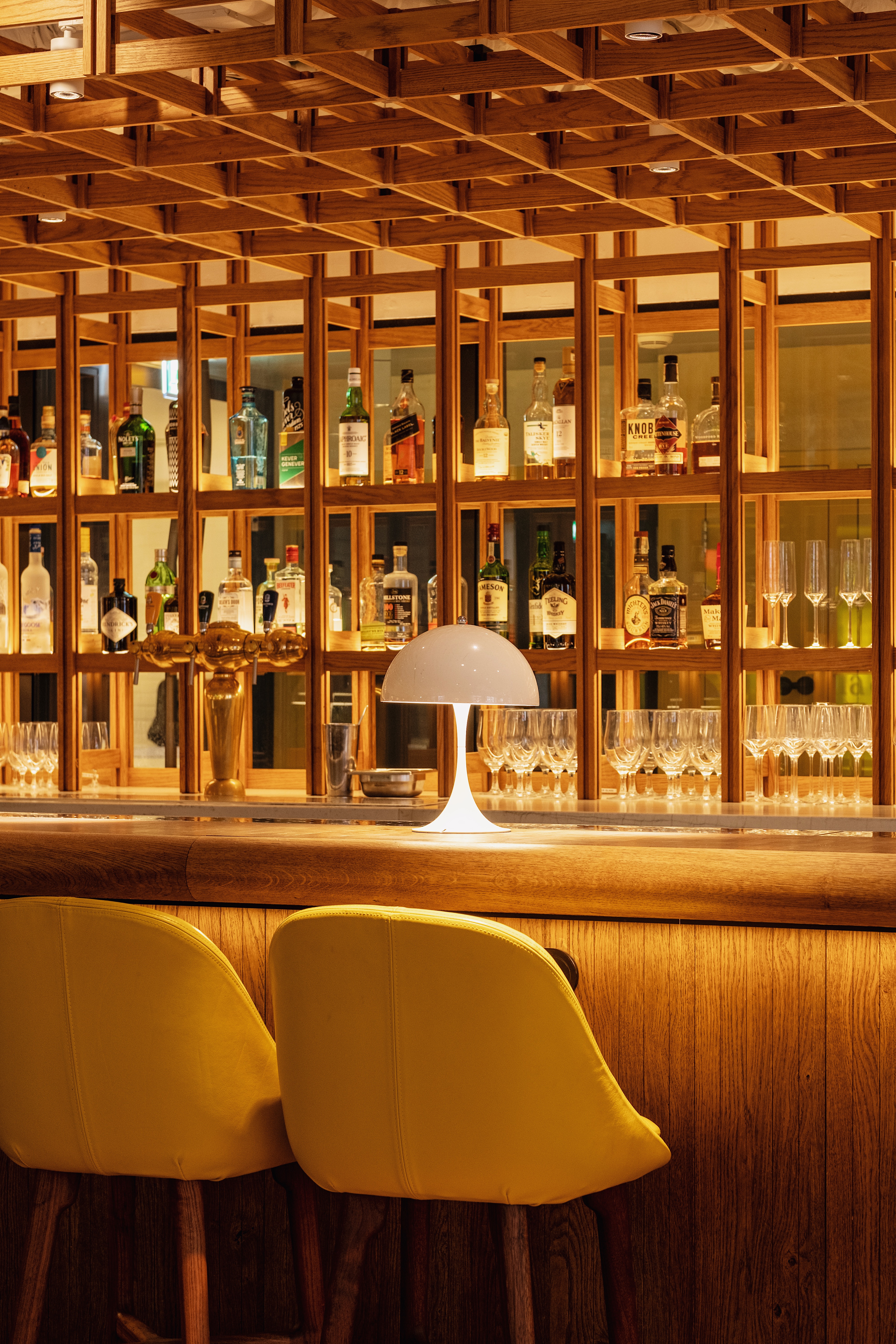 A bar scene with shelves of bottles and glassware, illuminated by soft lighting at the elegant Celia Amsterdam.