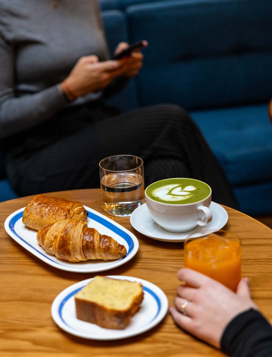 A close-up of coffee and baked goods, including croissants and lemon cake, on a wooden table at Café Celia Amsterdam.