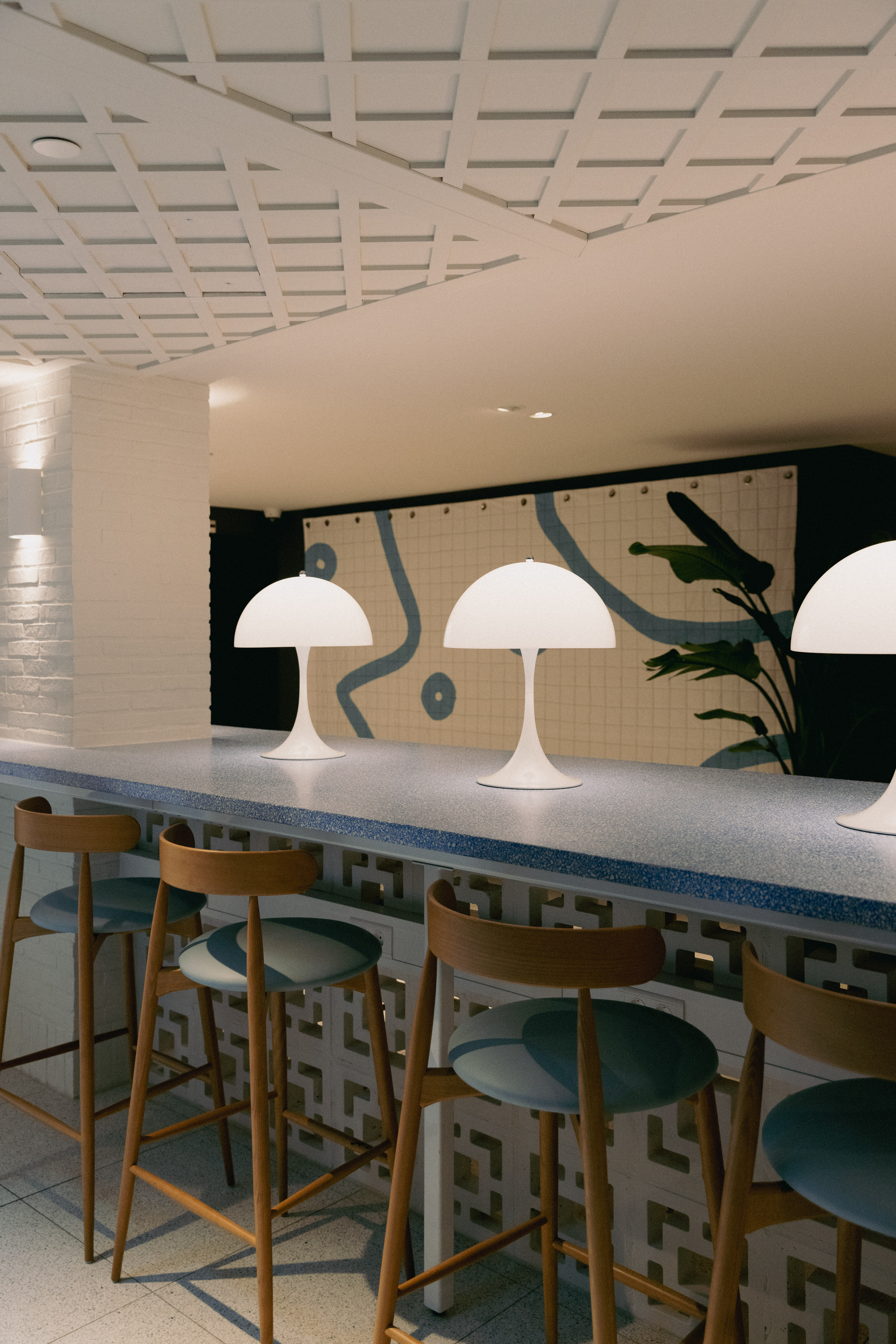 Modern bar with white lamps and wooden stools against a geometric tiled wall at Café Celia in Amsterdam.