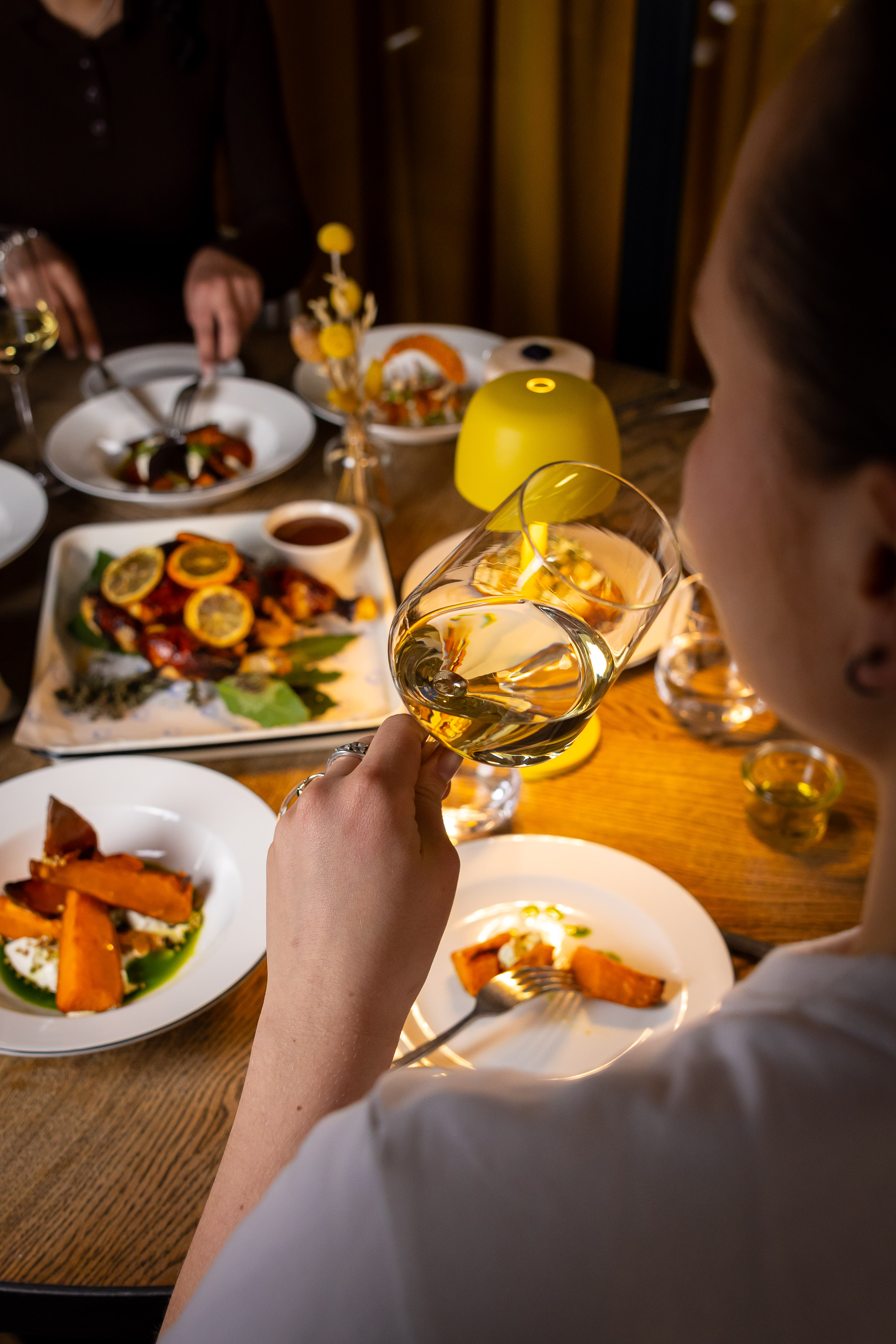 A person holding a wine glass over a table with various dishes at the relaxing Celia restaurant in Amsterdam.